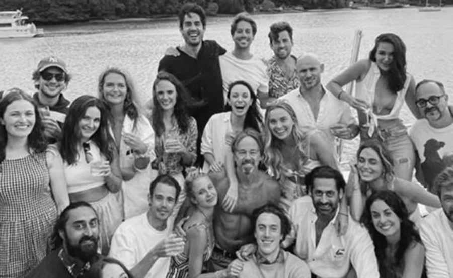 Group of friends smiling and posing on a boat, with a scenic river view in the background, in black and white.