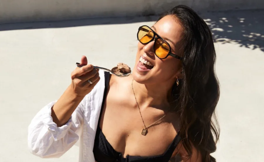 Woman wearing sunglasses enjoys a spoonful of chocolate ice cream under the sun.