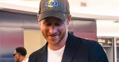 "Man in a baseball cap smiling indoors, casual attire, slight profile view."