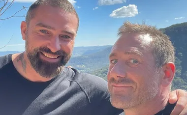 Two men smiling outdoors with scenic mountain view in the background.
