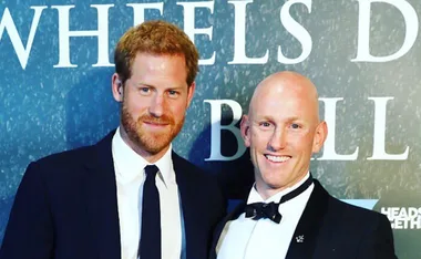 Two men in suits smiling at an event, with blue background and white text partially visible.