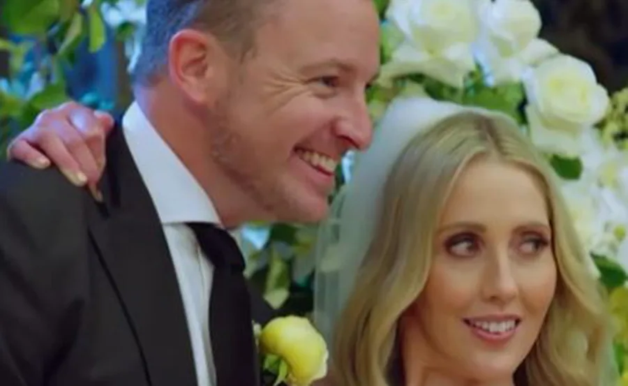 A smiling couple at a wedding, with white roses in the background.