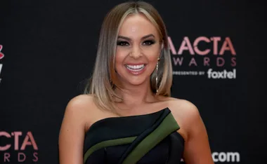 Person smiling on the AACTA Awards red carpet, wearing a black and green dress with large earrings.