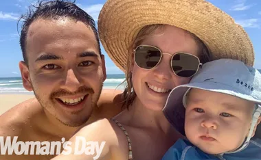 Family enjoying a sunny day at the beach; parents smiling with baby wearing a hat.