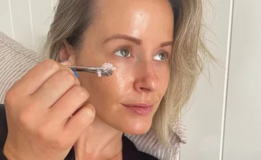 Applying skincare cream under eyes with tool.