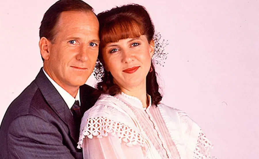 Couple in formal attire, woman in lacy dress with flowers in hair, man in suit, celebrating their wedding anniversary.