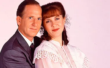 Couple in formal attire, woman in lacy dress with flowers in hair, man in suit, celebrating their wedding anniversary.