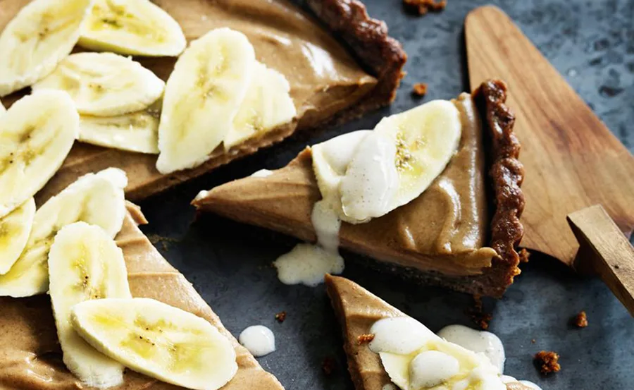 Banana cream pie slices with fresh banana toppings and cream on a wooden board.