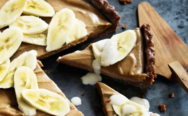 Banana cream pie slices with fresh banana toppings and cream on a wooden board.