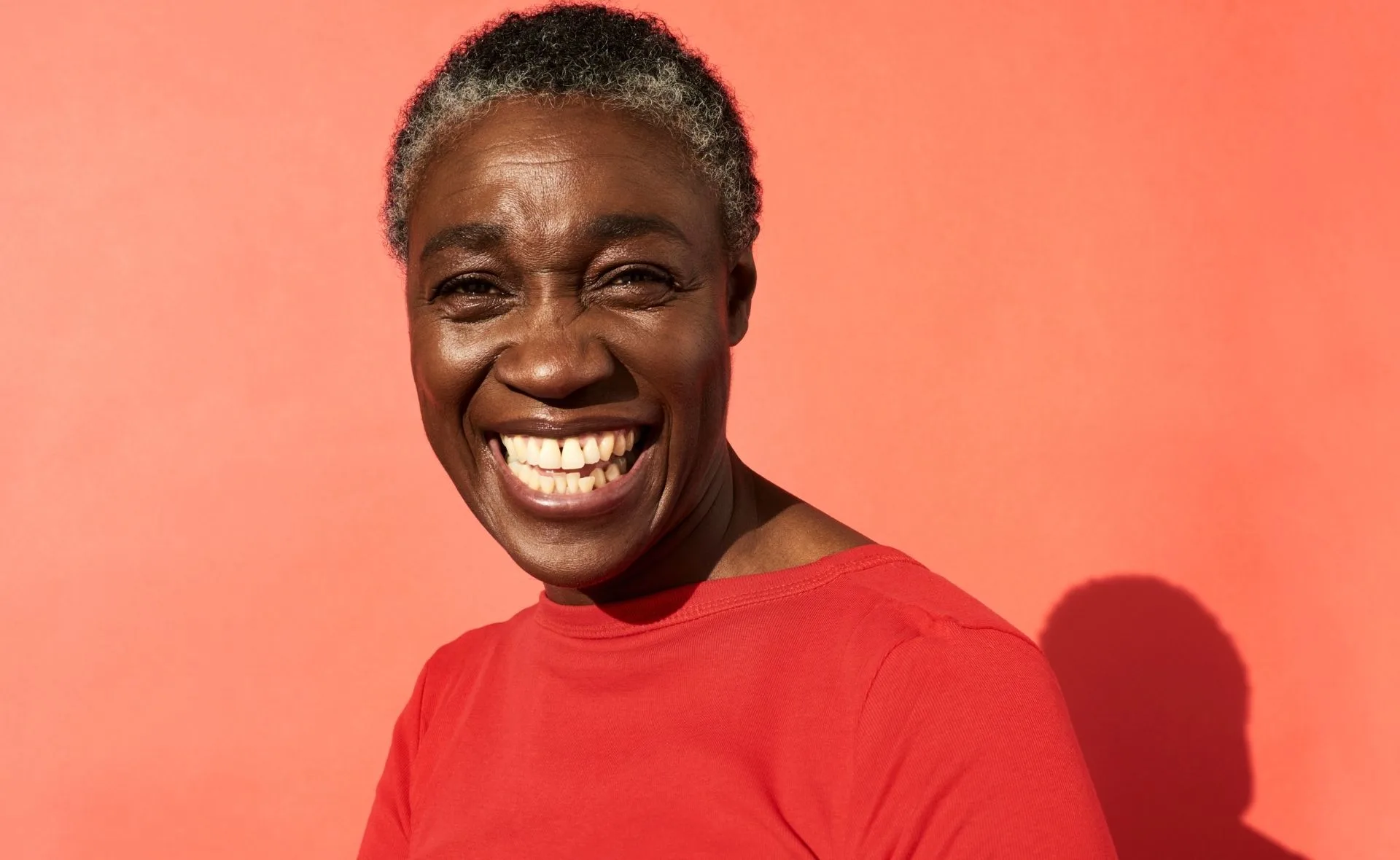 Smiling woman in a red shirt against a bright red background.