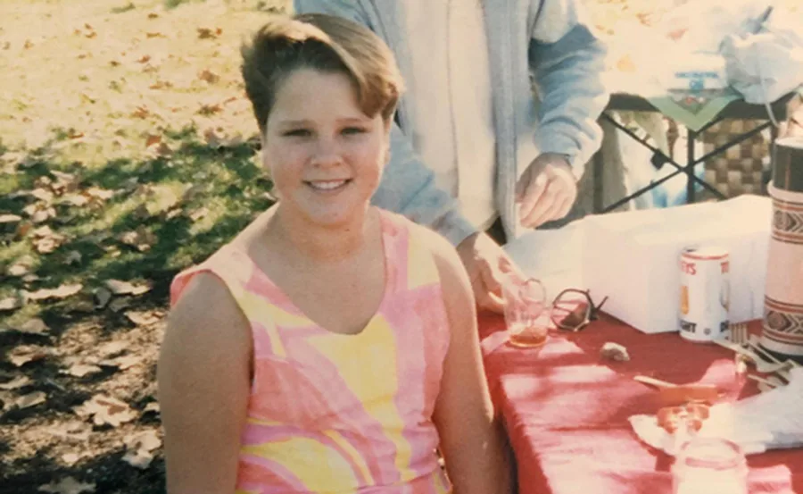 Young person smiling in a colorful dress at an outdoor event with picnic setup.