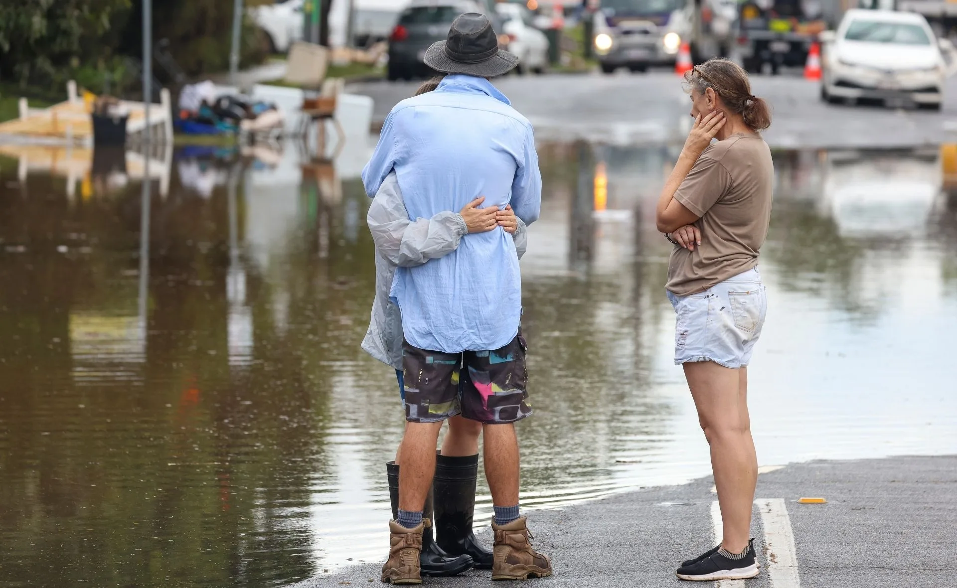 Three people stand on a flooded street, two embracing, the third looking on thoughtfully.