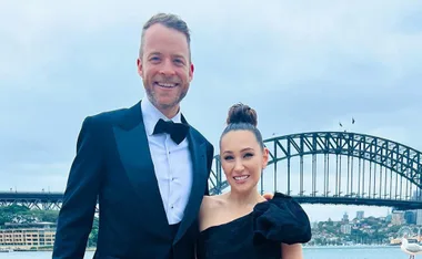 Couple in formal attire smiling in front of Sydney Harbour Bridge.