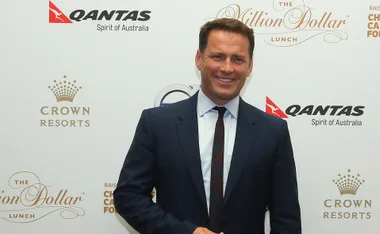 A man in a suit smiles at a Million Dollar Lunch event backdrop with Qantas and Crown Resorts logos.