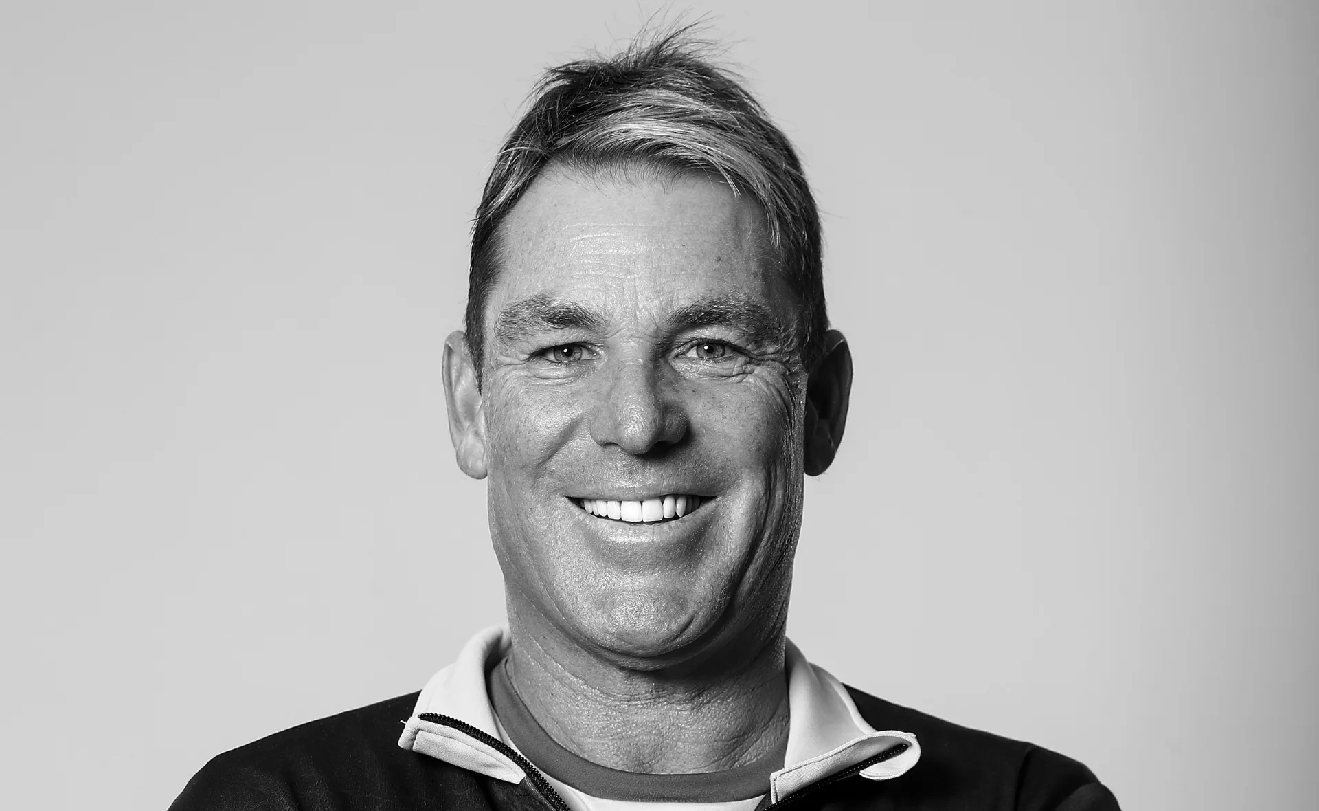 Monochrome portrait of a smiling man with short hair, wearing a collared jacket.
