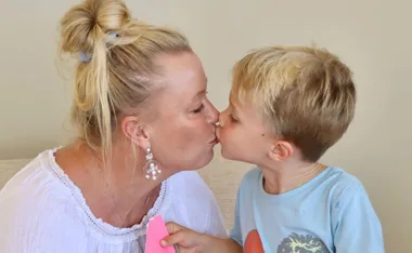 Grandmother shares a tender kiss with her young grandson, who holds a pink paper in his hand.