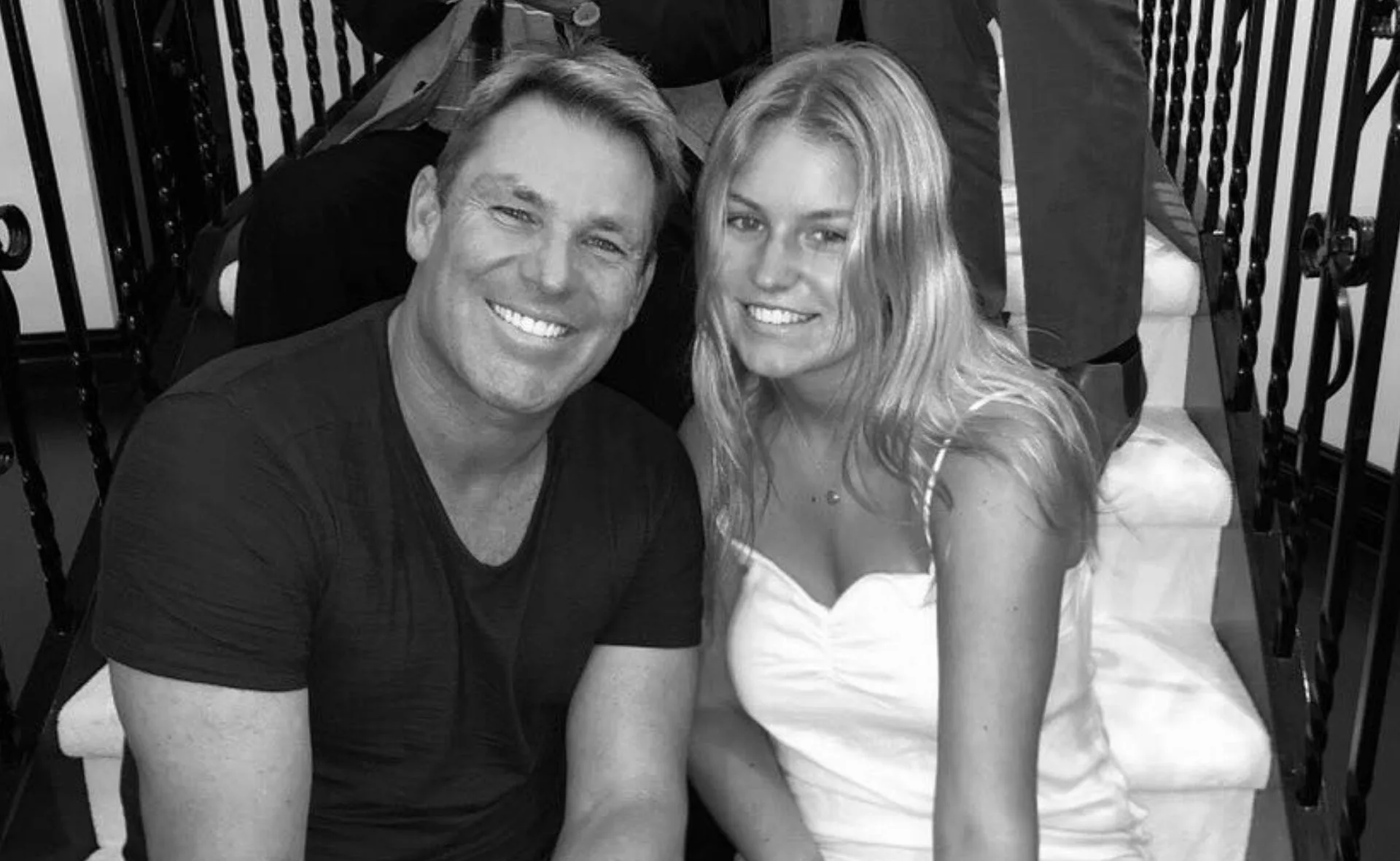 A smiling man and woman sit together on a staircase in black and white.