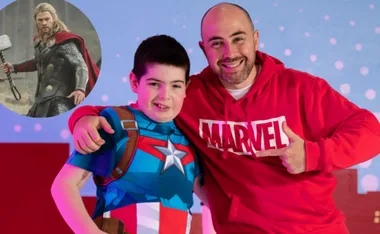 Two people smiling, one in a Captain America outfit, with a Thor character image in the background.