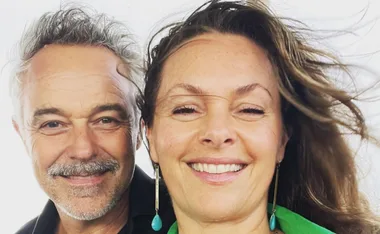 A smiling couple with windswept hair, close-up portrait.