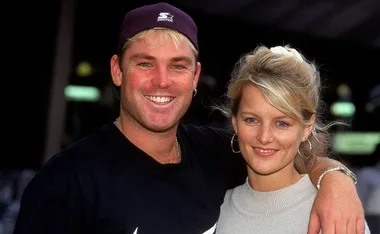 Two people smiling outdoors, one wearing a cap and the other with earrings and a watch.
