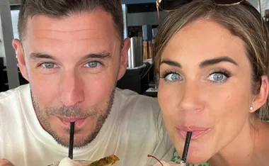 Couple sharing a drink with straws, smiling at the camera.