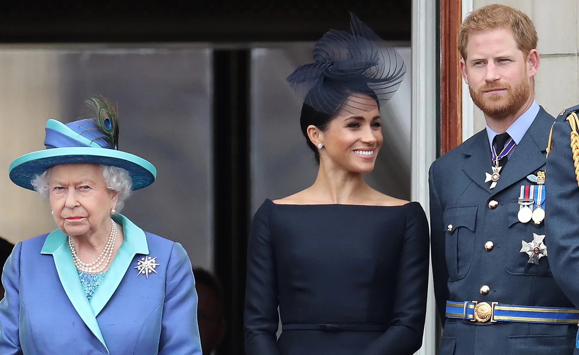 Queen Elizabeth II, Meghan Markle, and Prince Harry standing together at an event, all dressed formally.