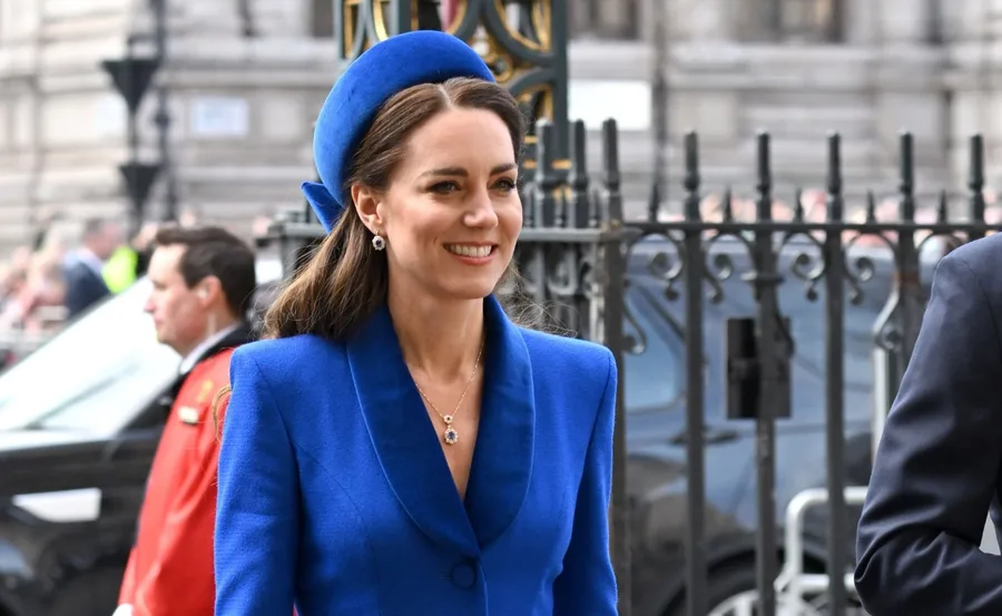 Kate Middleton in a royal blue outfit and matching hat at a public event outside a historic building.