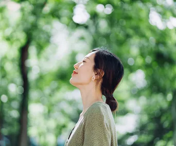 A woman enjoys a serene moment, eyes closed, in a lush green forest.