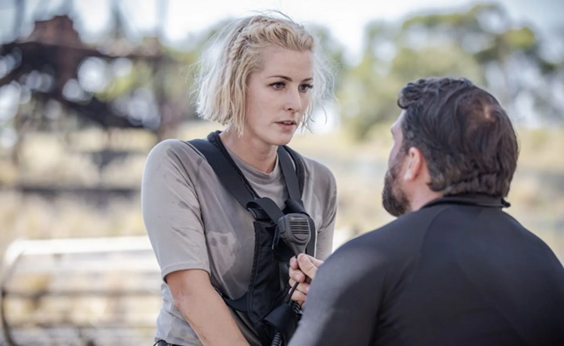 Two individuals in tactical gear have an intense conversation outdoors.