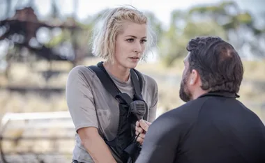 Two individuals in tactical gear have an intense conversation outdoors.