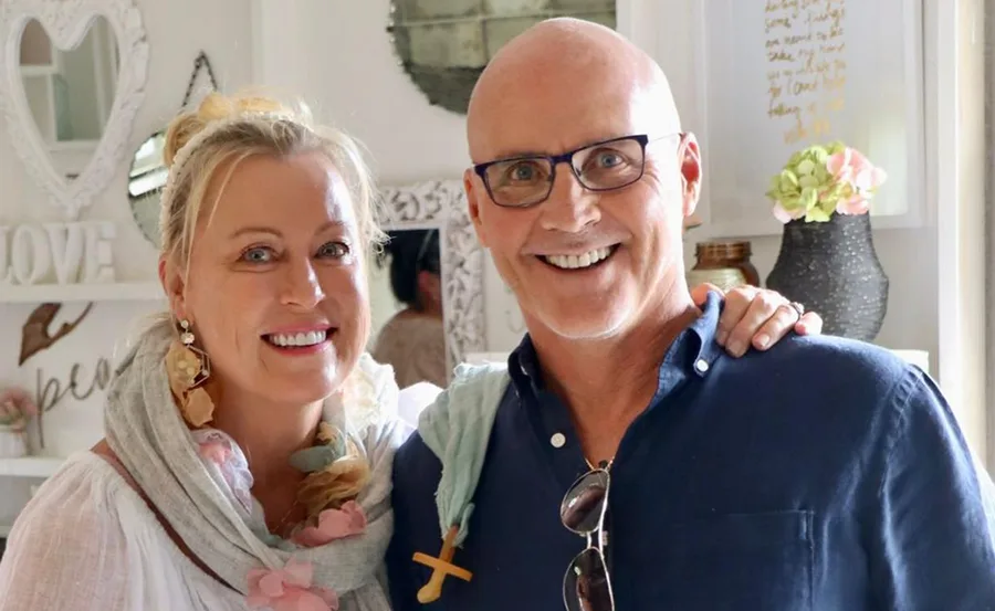 A couple smiling together indoors, with decorative wall art in the background.