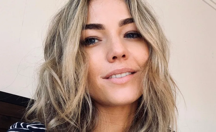 Portrait of a woman with wavy blonde hair, subtle makeup, smiling slightly.