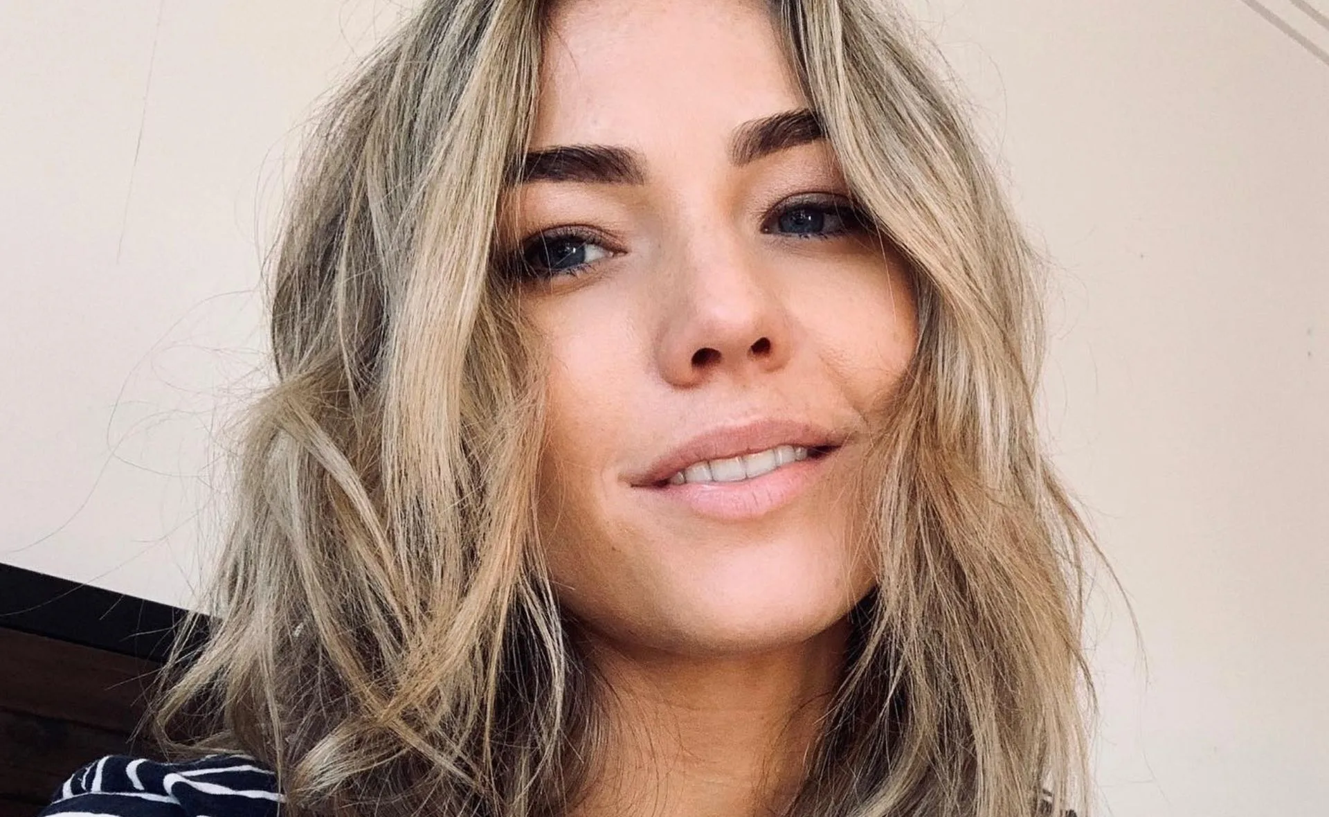 Portrait of a woman with wavy blonde hair, subtle makeup, smiling slightly.