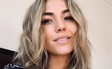 Portrait of a woman with wavy blonde hair, subtle makeup, smiling slightly.