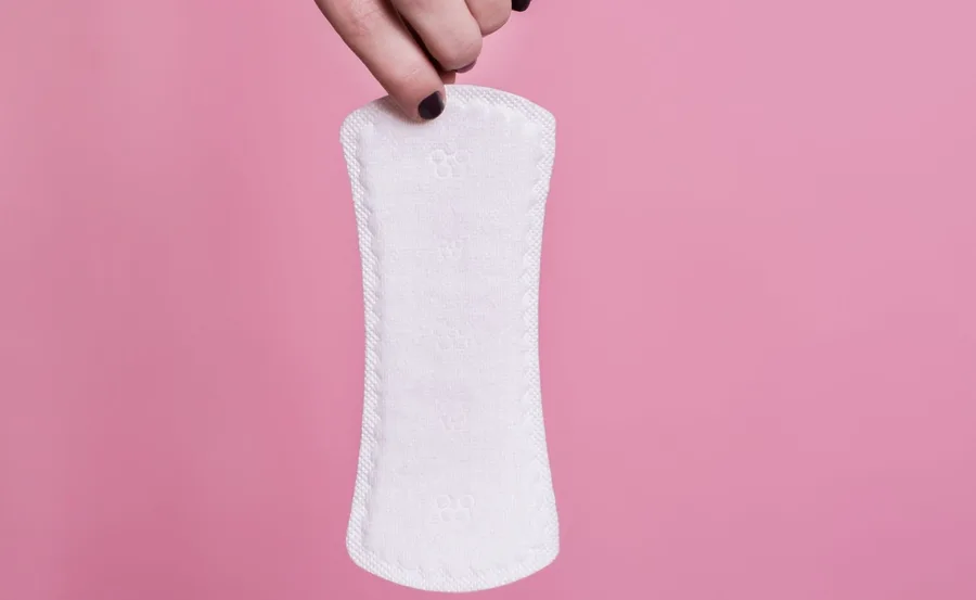 Hand holding a white biodegradable menstrual pad against a pink background.