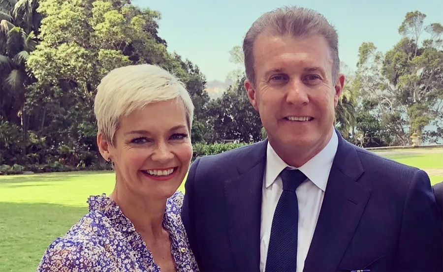 A couple smiling outdoors with trees in the background.