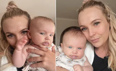Mother holding baby girl, both smiling, indoors. Baby wearing floral outfit and mother with long blonde hair.