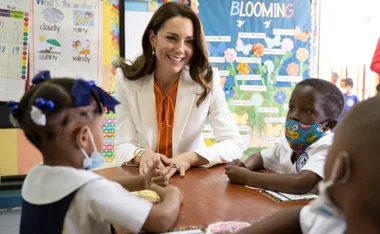 Kate Middleton interacts with schoolchildren in a classroom setting in Jamaica, engaging in conversation.