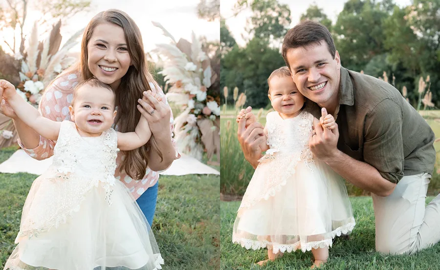Mother and father joyfully holding their toddler in a garden setting, celebrating the child's first birthday.
