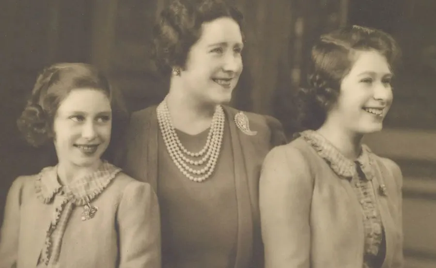 A vintage photo of a mother with her two daughters, all smiling, wearing formal attire with pearls and brooches.