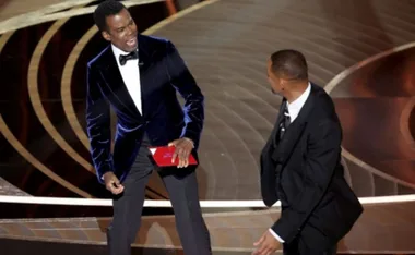 Two men on stage at an awards show, one holding an envelope.