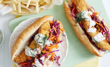 Fish sandwiches with crispy fillets, coleslaw, and sauce on bread, with a side of fries.