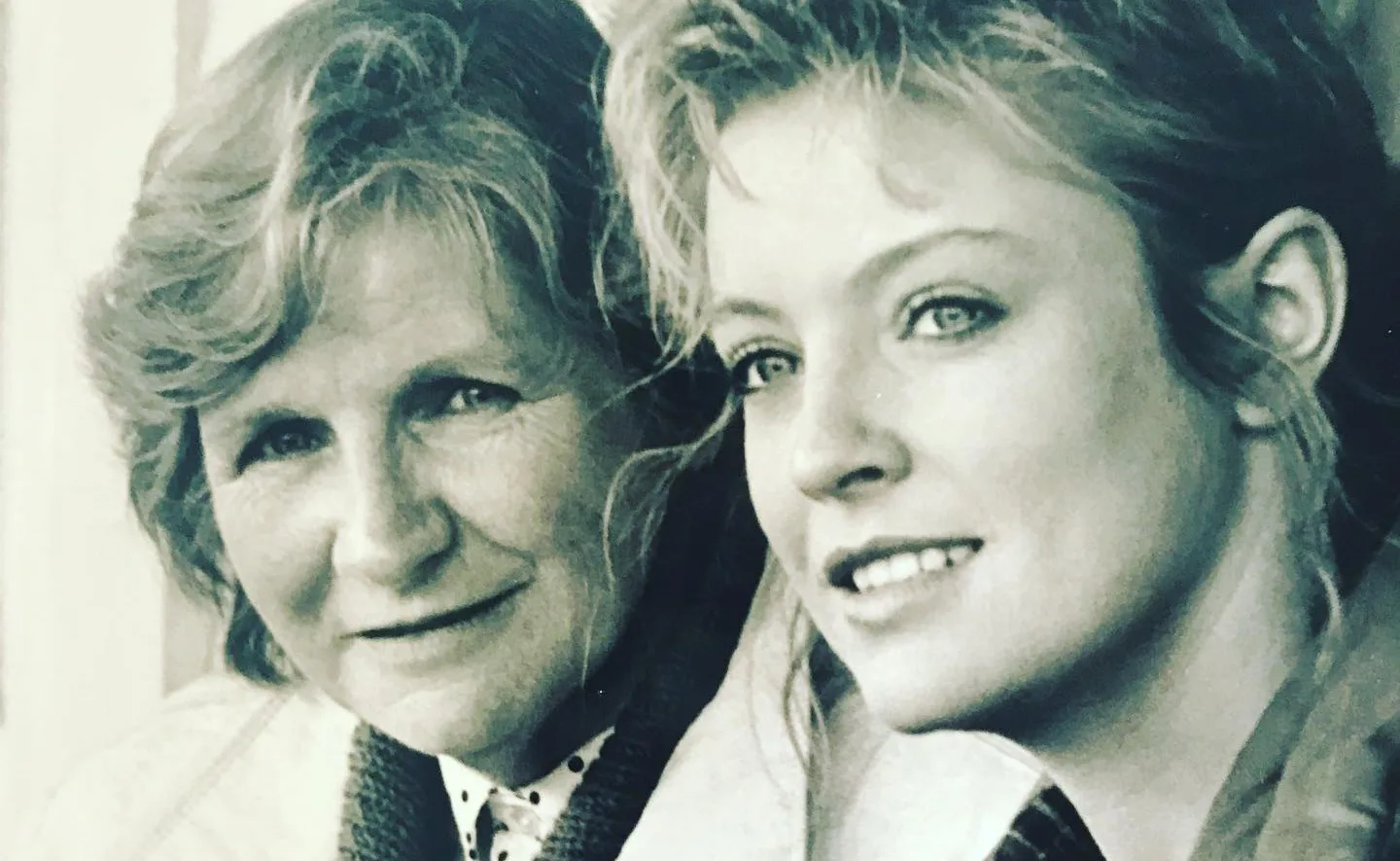 Two women smiling in a black and white photo, one older on the left and one younger on the right.