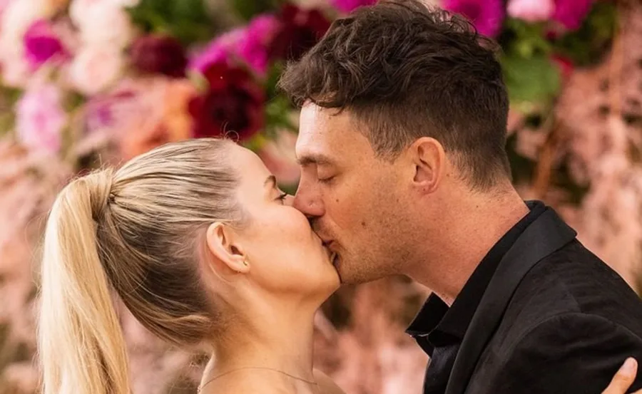 A couple kissing passionately in front of a colorful floral background.