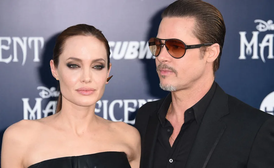 Two people at a movie premiere event, standing in front of a "Maleficent" themed backdrop.
