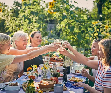 Group of women clinking glasses at an outdoor picnic table surrounded by sunflowers.