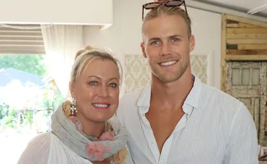 A man and a woman smiling together indoors, with the man wearing sunglasses on his head.