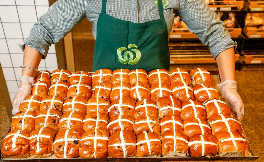 Person holding a tray of fresh hot cross buns at a Woolworths store.