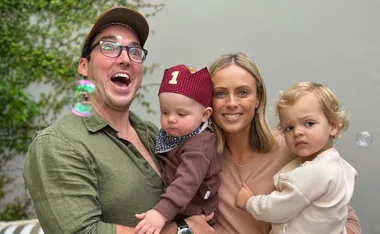 Man and woman smiling with two children; one child wears a birthday hat with "1" on it, and bubbles float around them.