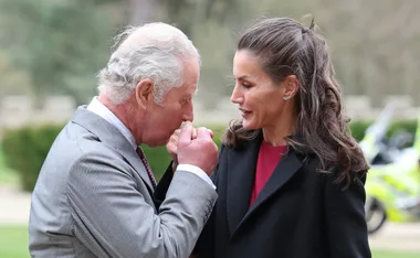 Man in suit kisses woman's hand outdoors, both smiling.